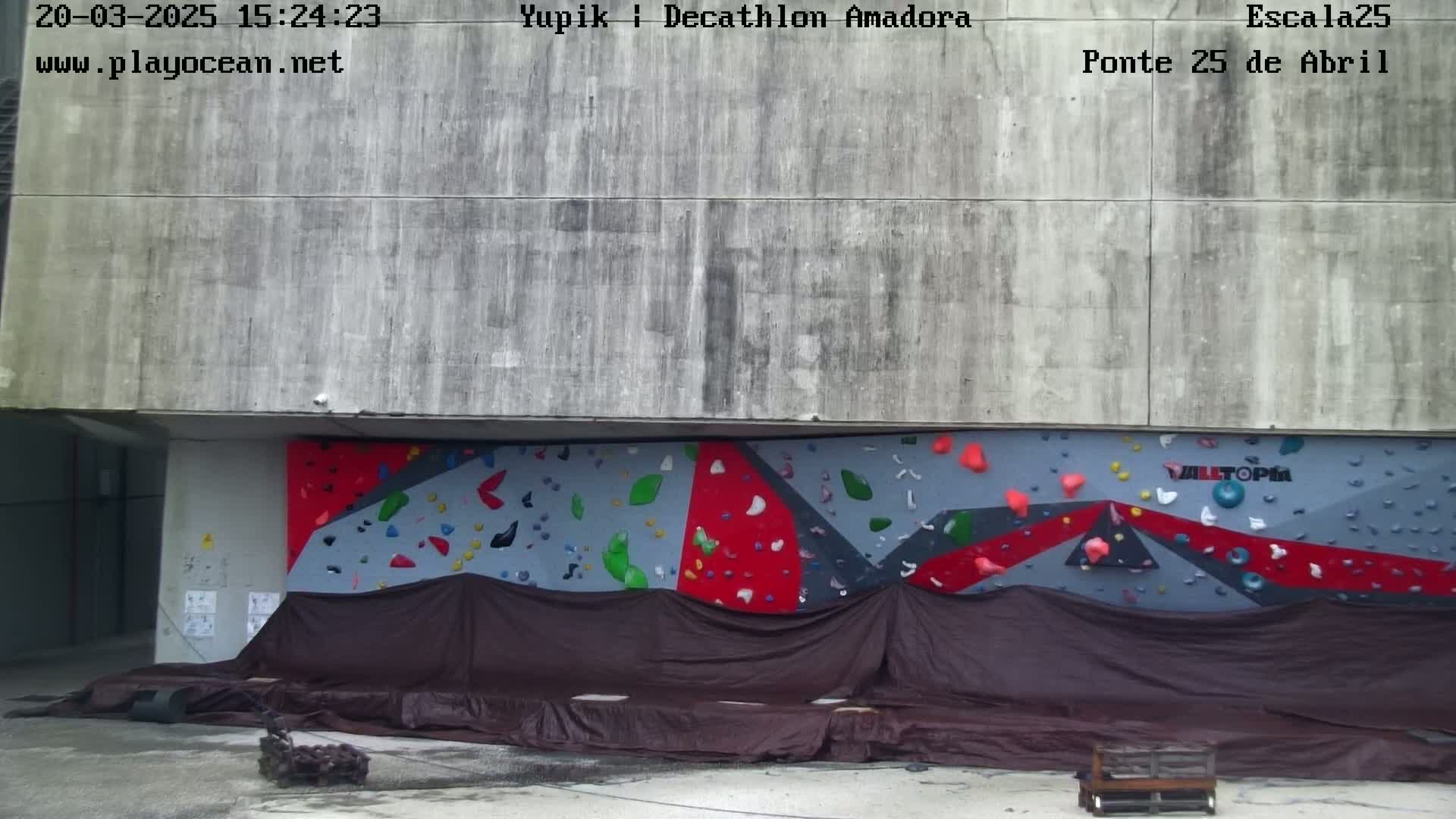 A partially covered outdoor climbing wall is situated against a concrete building.