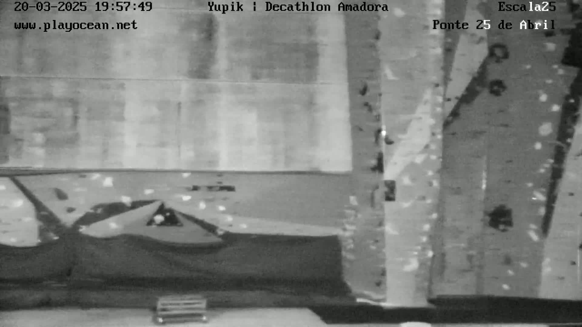 A grayscale image shows an indoor climbing wall with various holds and a small object resembling a bench at the bottom.