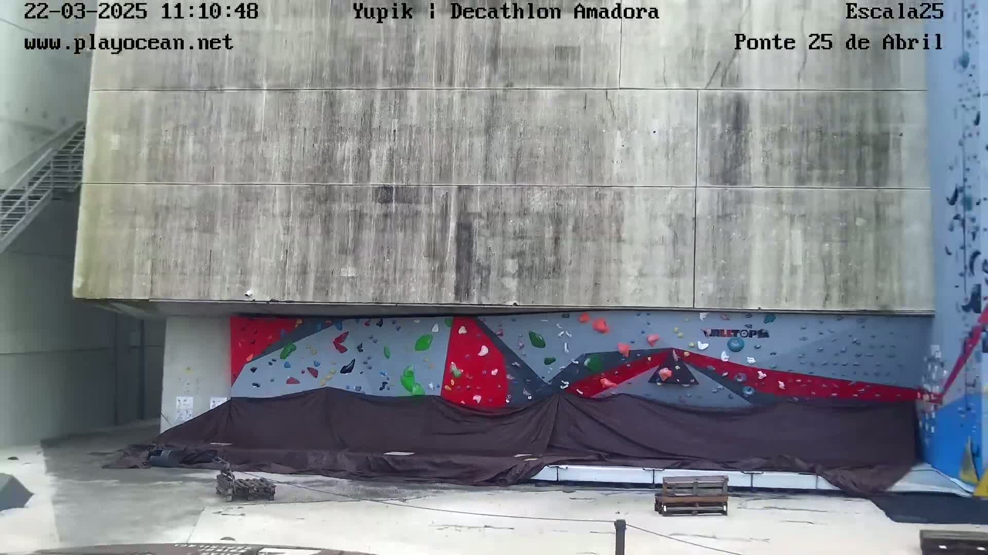 A partially covered outdoor climbing wall is situated against a large concrete building.