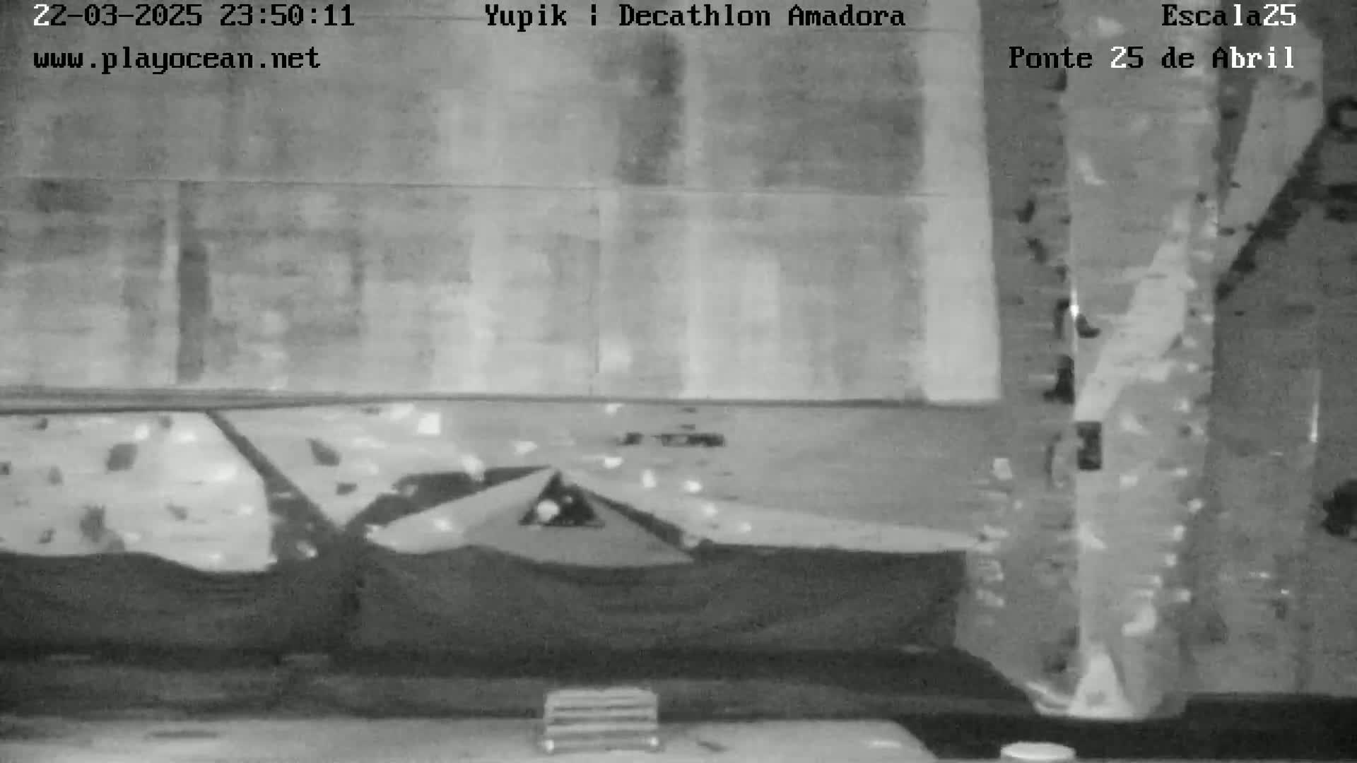 A grayscale image shows an indoor climbing wall with several dark, possibly fabric, objects at its base.