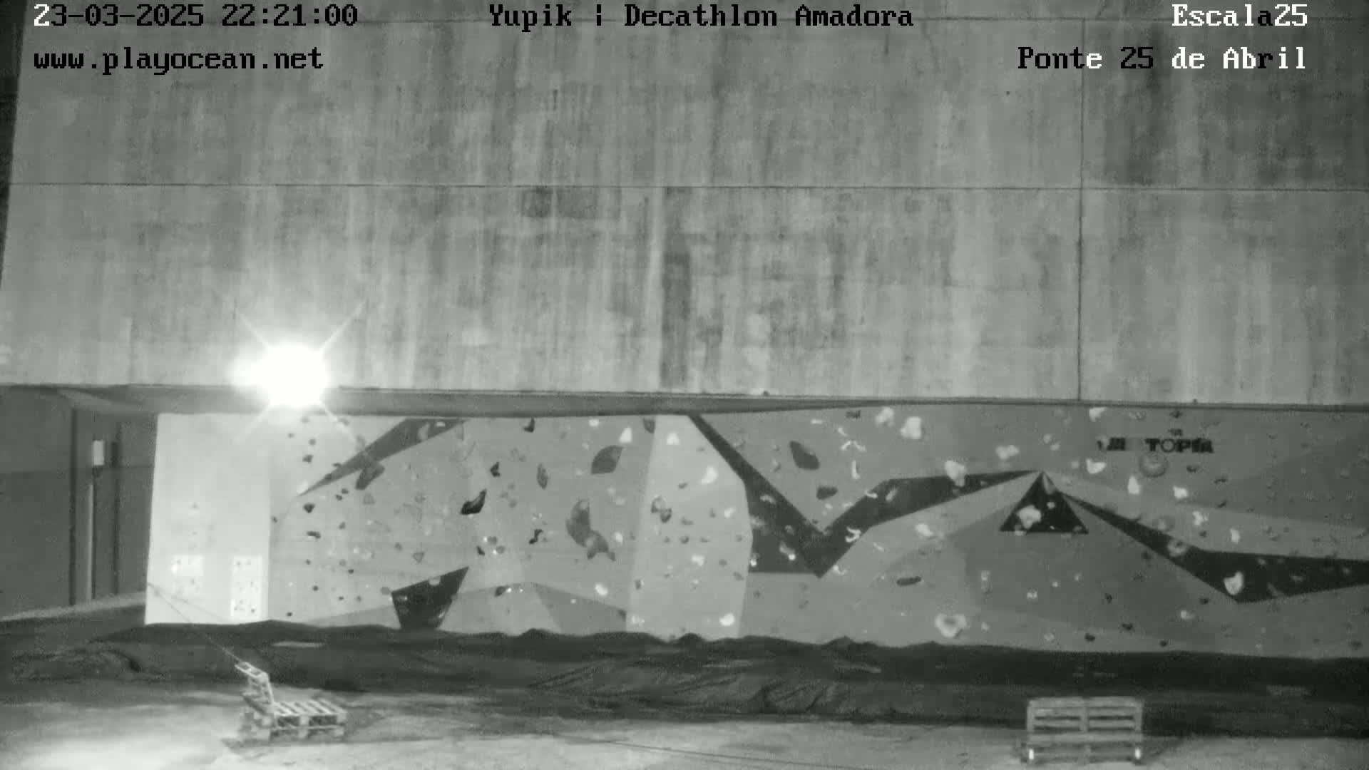 A nighttime, black and white image shows an outdoor climbing wall illuminated by a single light source.
