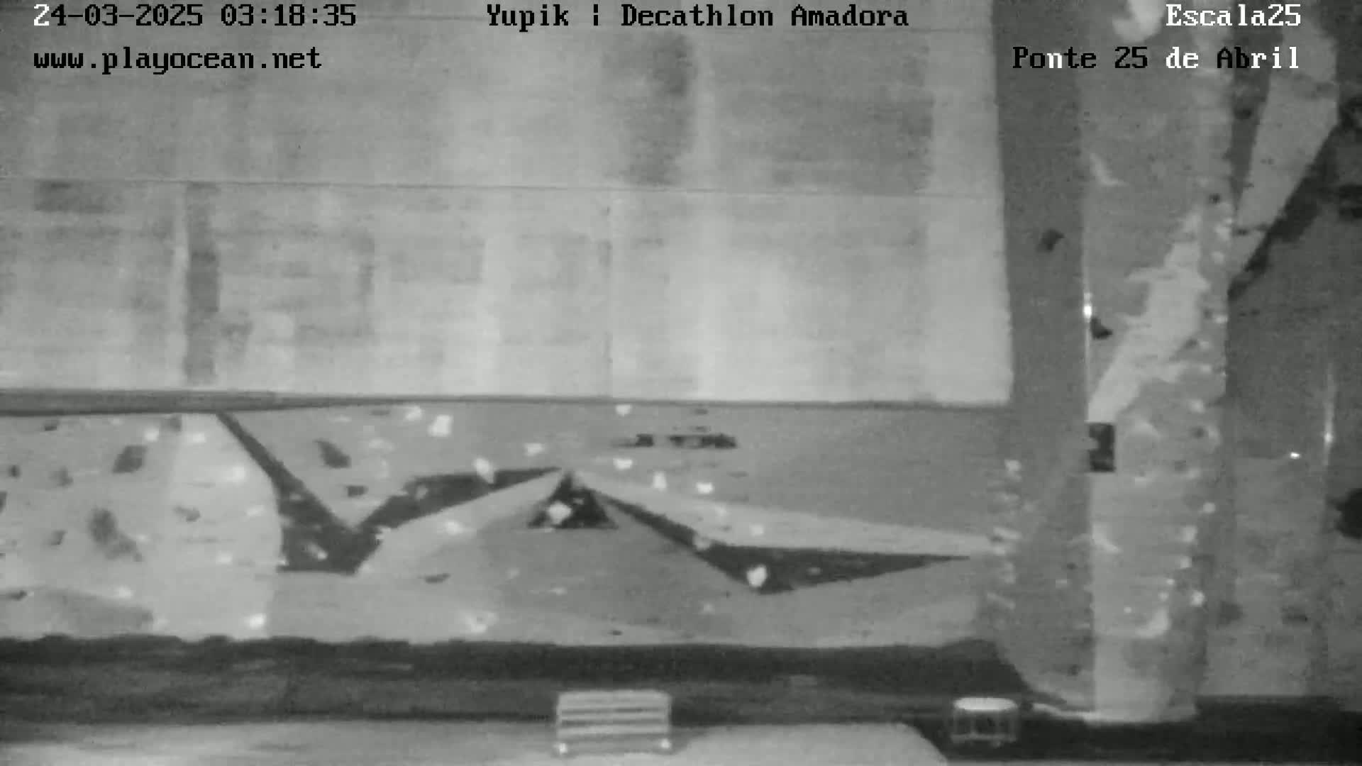 A grayscale image shows an indoor climbing wall with various holds and two small objects near the bottom.