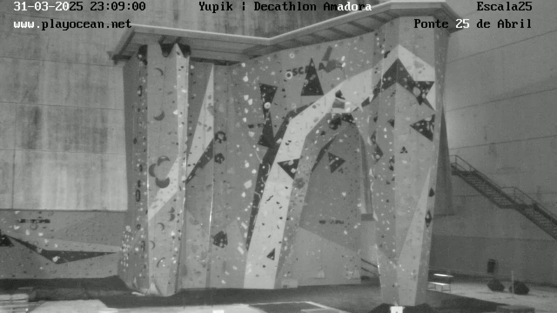 A large indoor climbing wall with various colored holds is situated in a dimly lit room.
