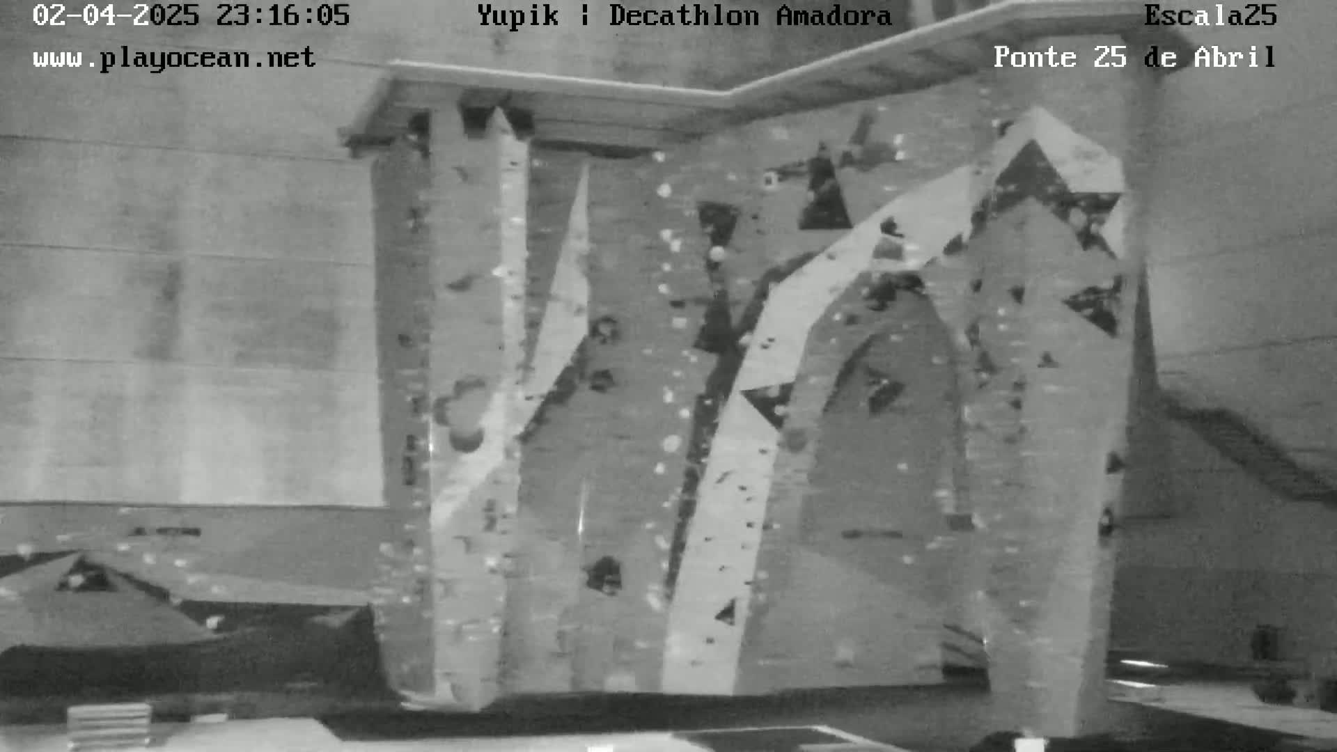 A grayscale image shows an indoor climbing wall with various holds and routes.