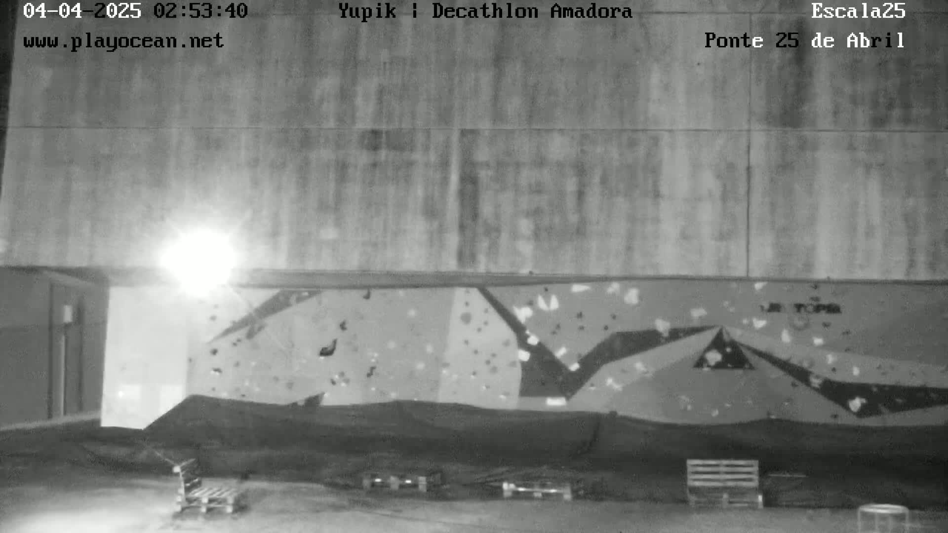 A nighttime, outdoor view of a climbing wall under a light, with several objects in the foreground.