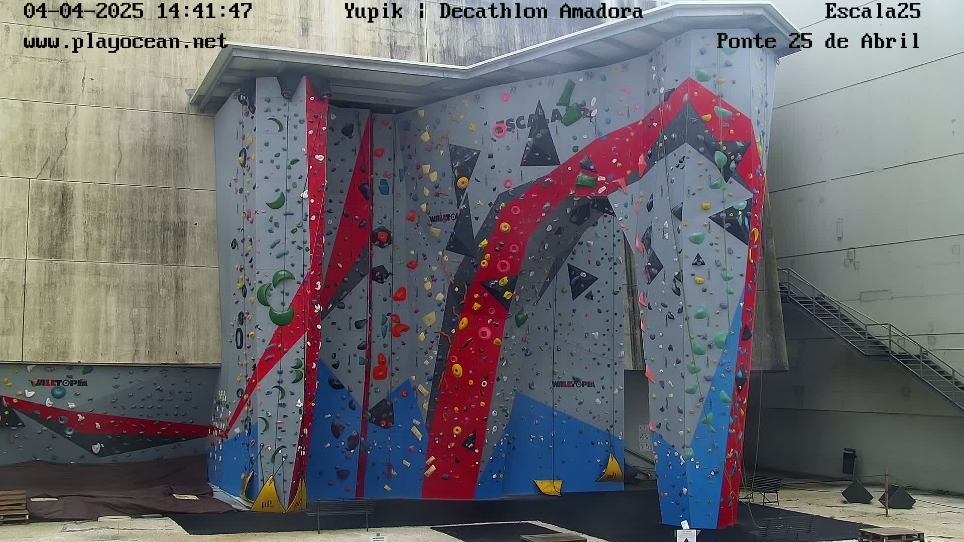 A large, multi-colored indoor climbing wall stands against a light gray building.