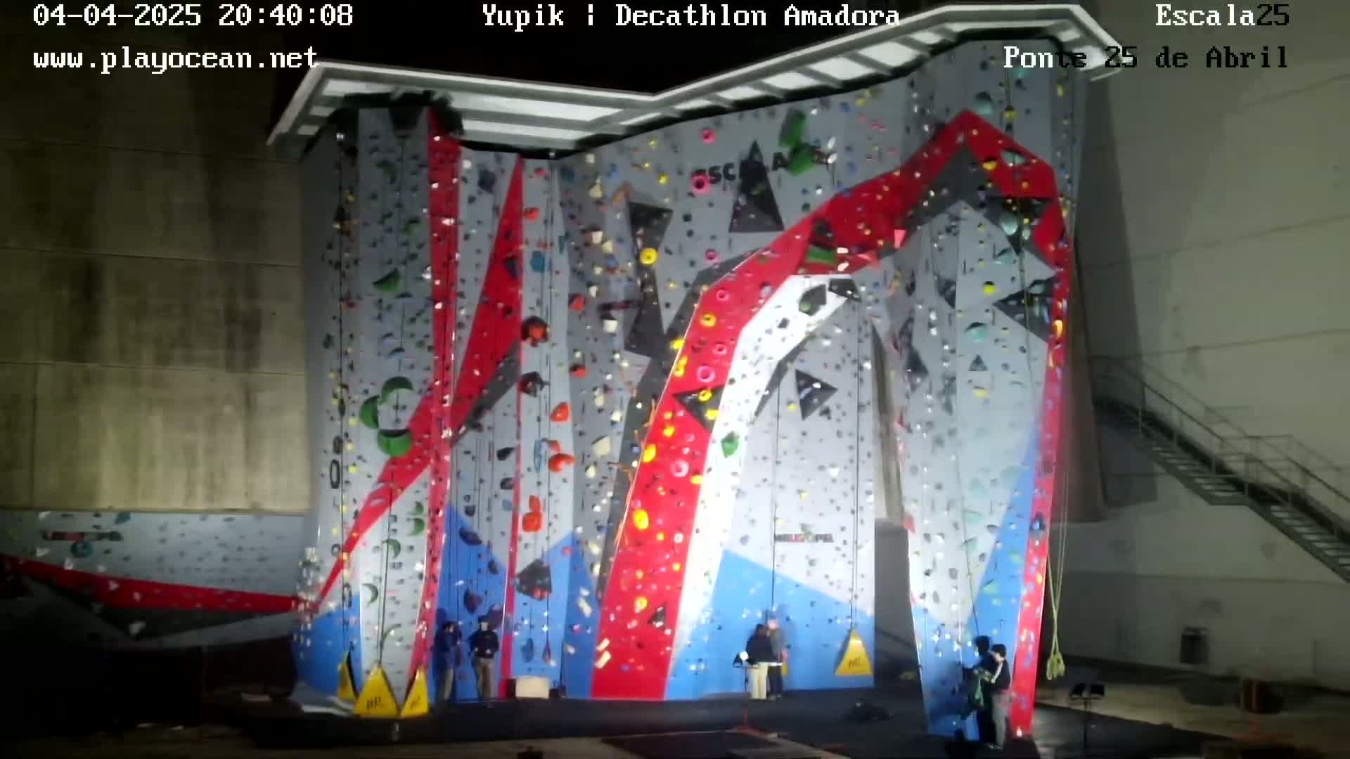 An indoor climbing wall with various colored holds is illuminated, and several people are standing at its base.