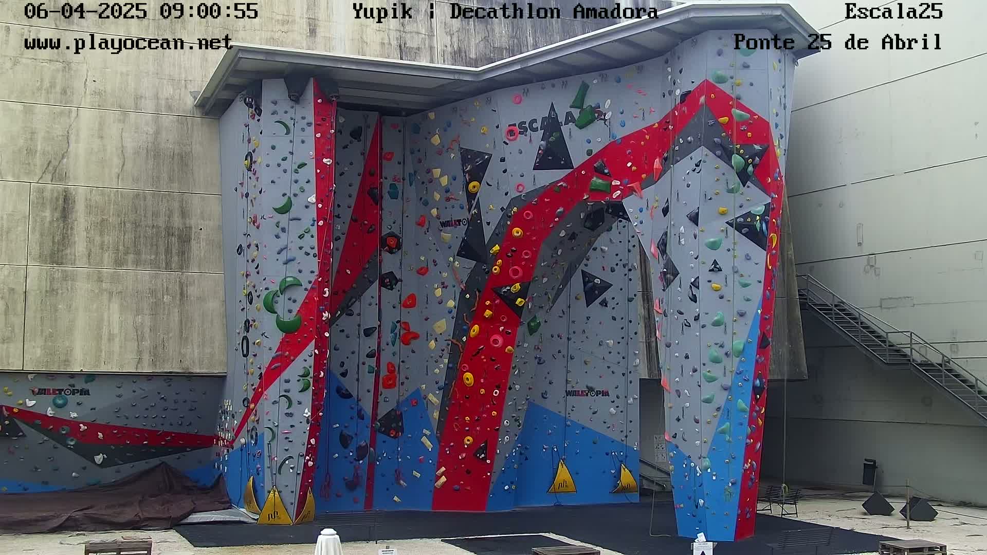 A large, colorful outdoor climbing wall stands against a building under overcast skies.