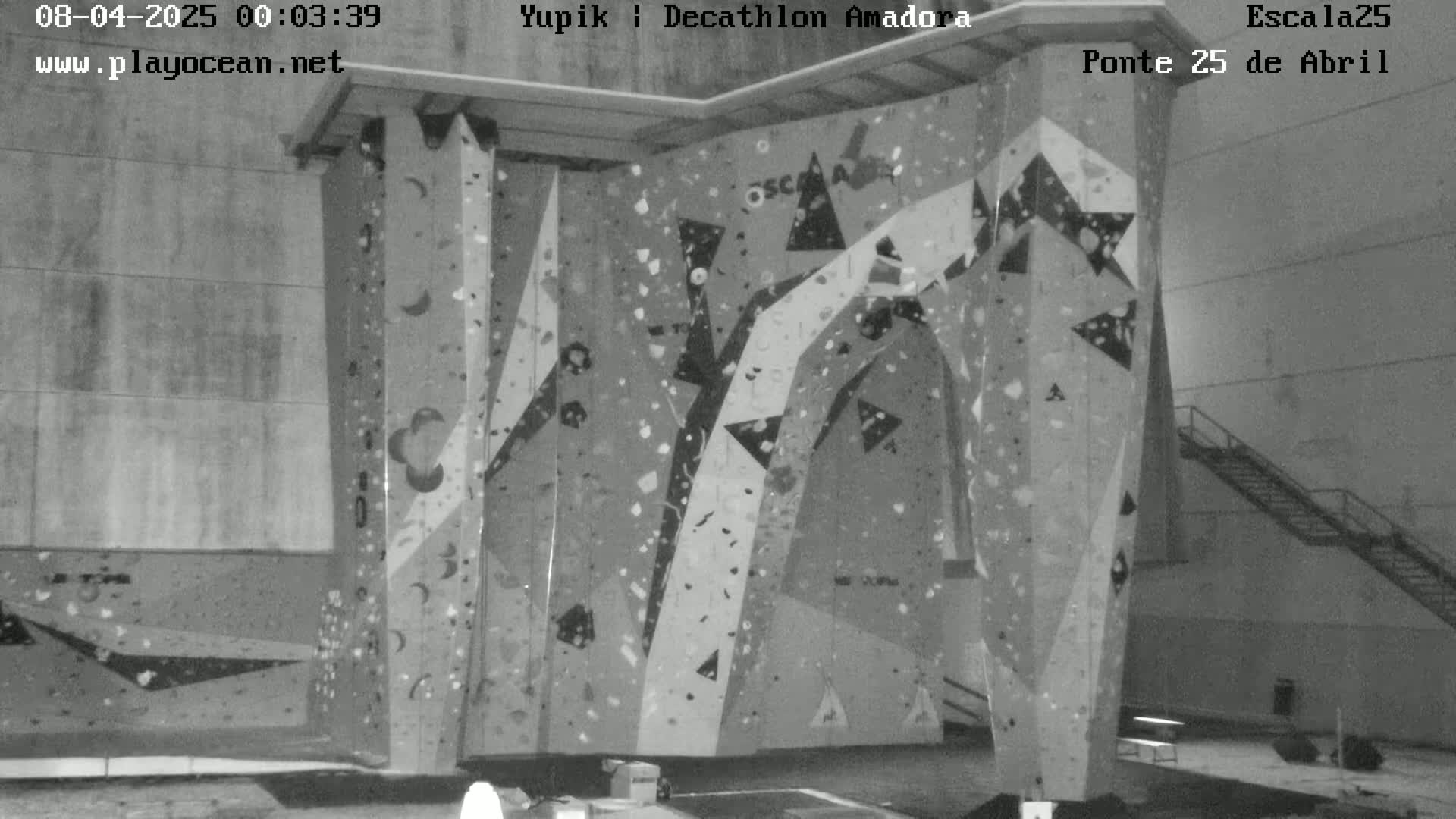 A grayscale image shows an indoor climbing wall with various holds and geometric designs.