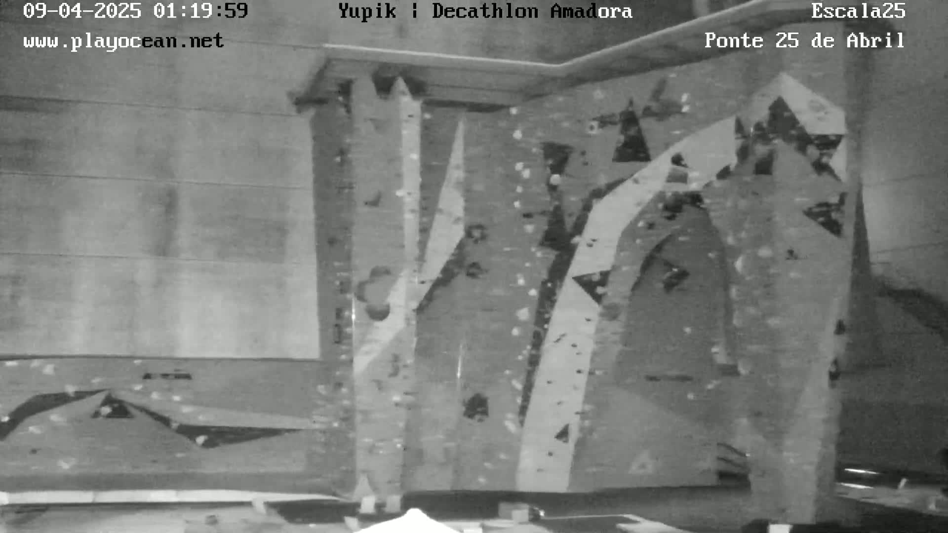 A grayscale image shows an indoor climbing wall with various holds and routes.