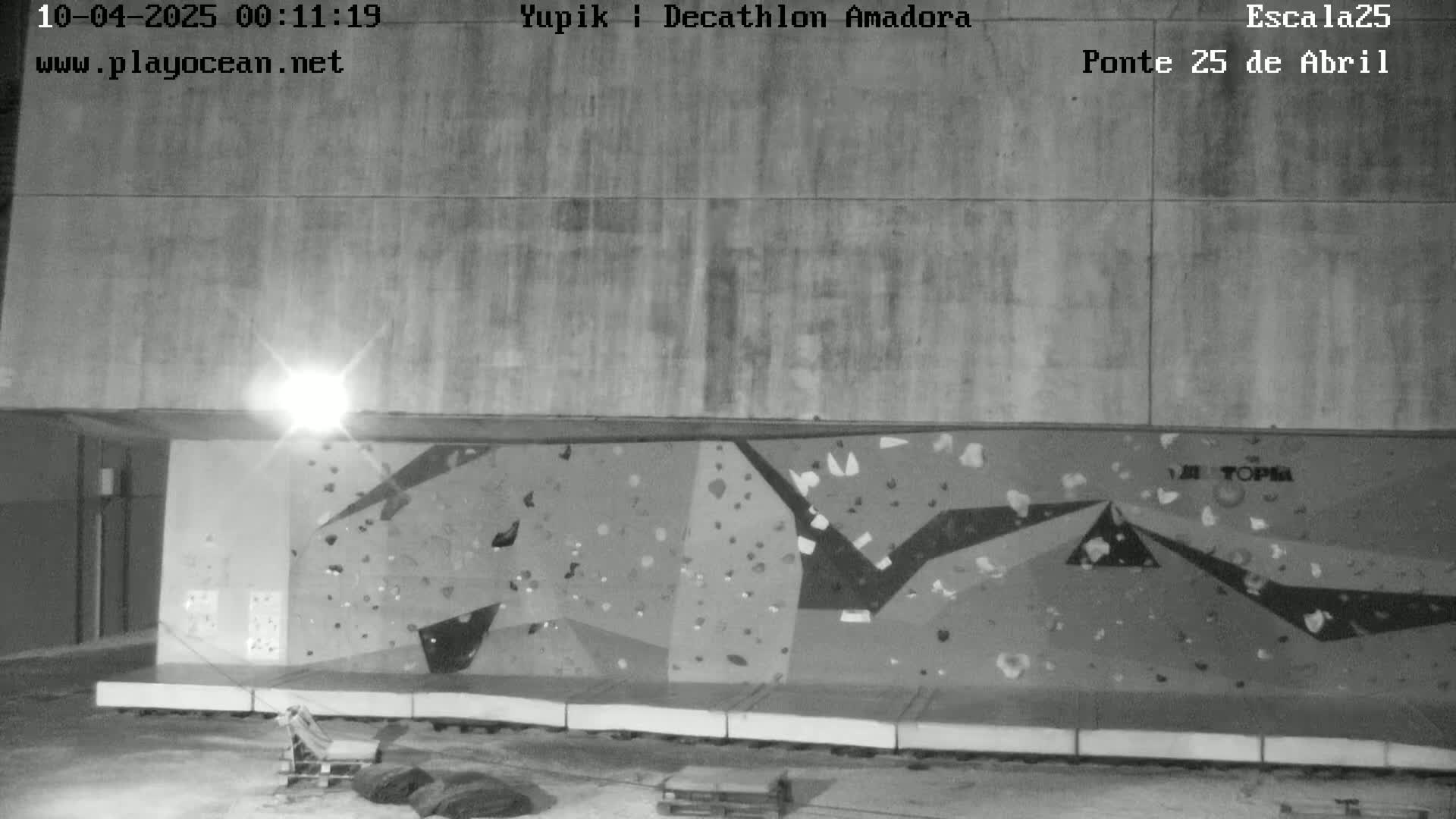 A nighttime, black-and-white image shows an outdoor climbing wall under a light source.