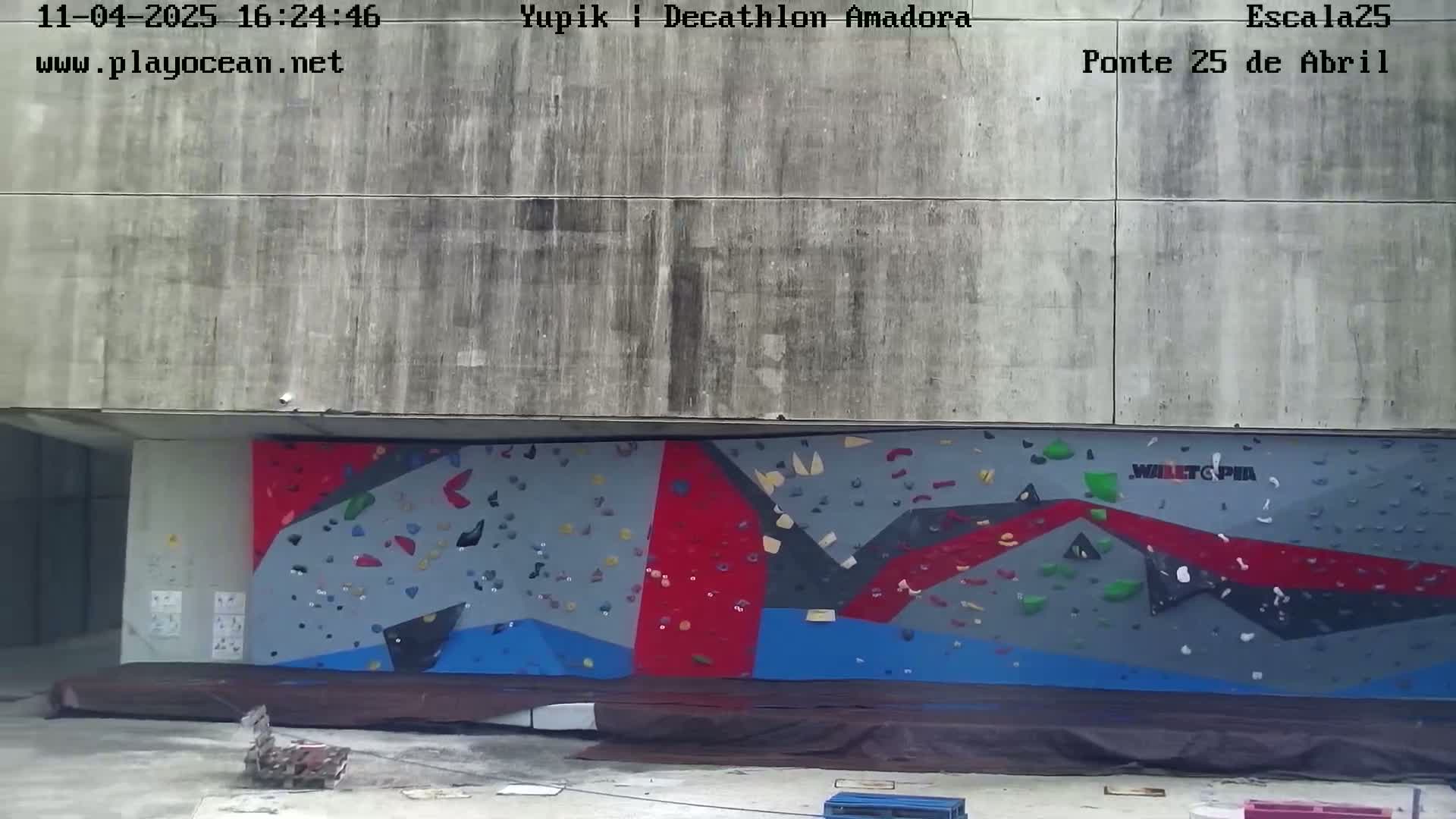 A large, colorful climbing wall is situated against a concrete building outdoors.