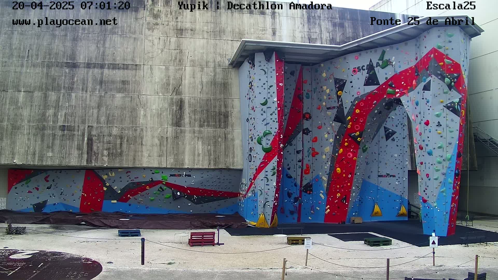 An outdoor view of a large, colorful climbing wall affixed to a building on a partly cloudy day.