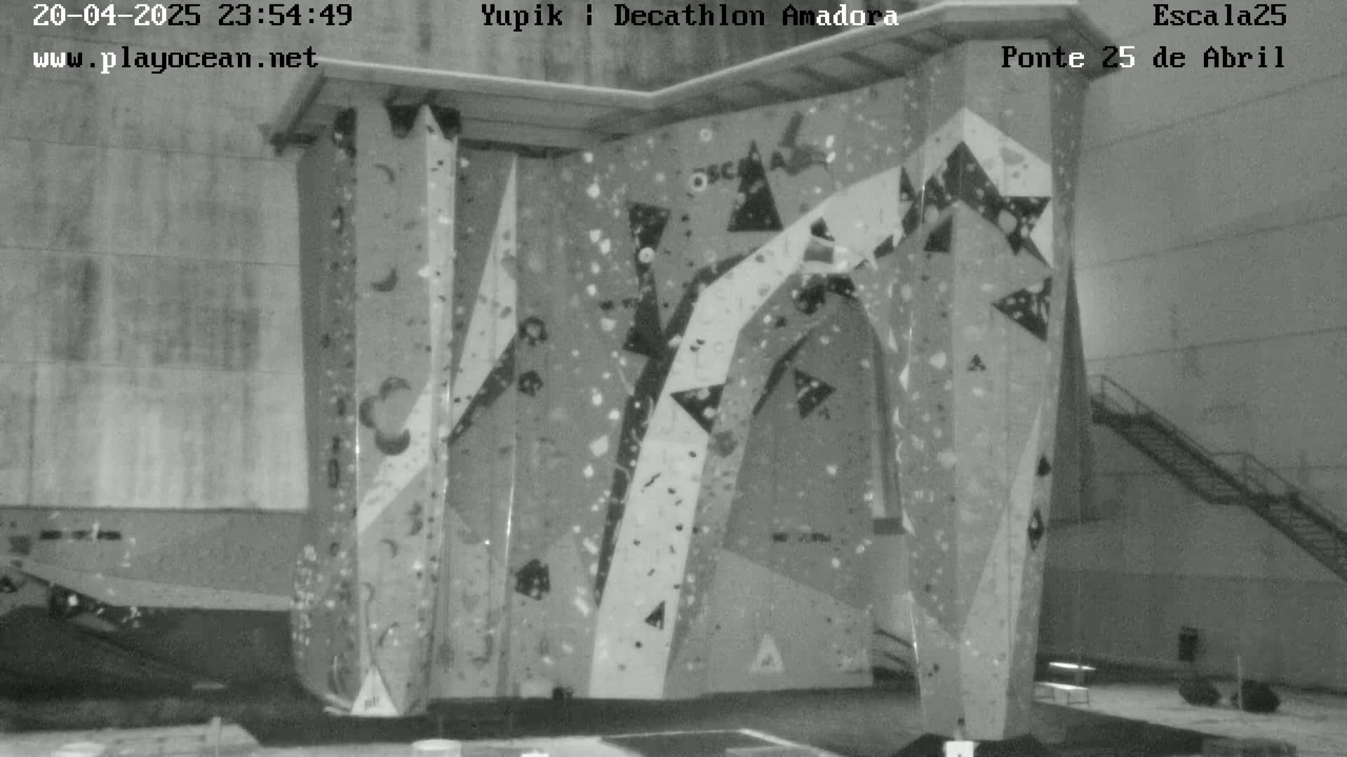 A large indoor climbing wall with various holds and angles is shown in a black and white image.