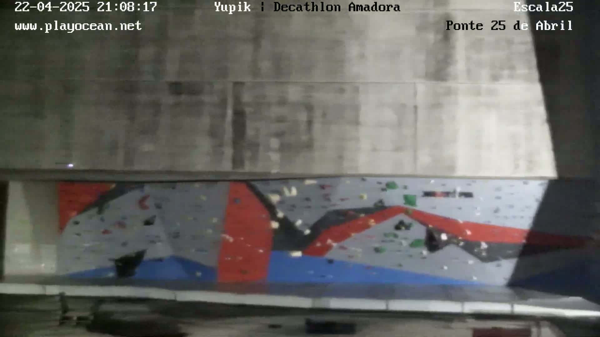An indoor climbing wall with various colored holds is visible under artificial lighting.