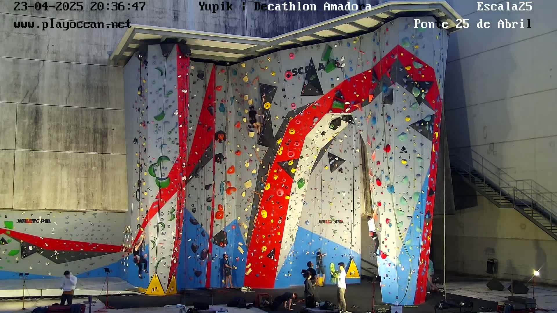 A large indoor climbing wall with various colored holds and several climbers scaling its surface.
