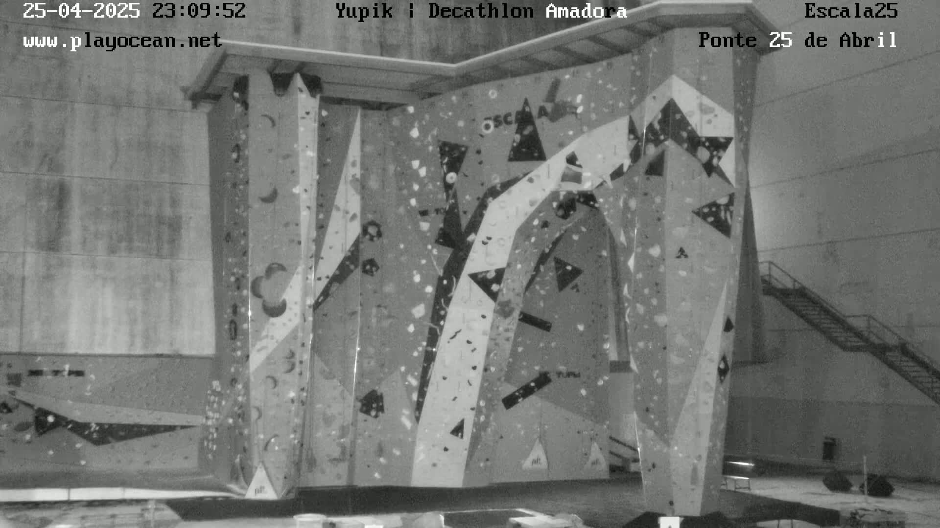 A grayscale image shows an indoor climbing wall with various holds and geometric patterns.