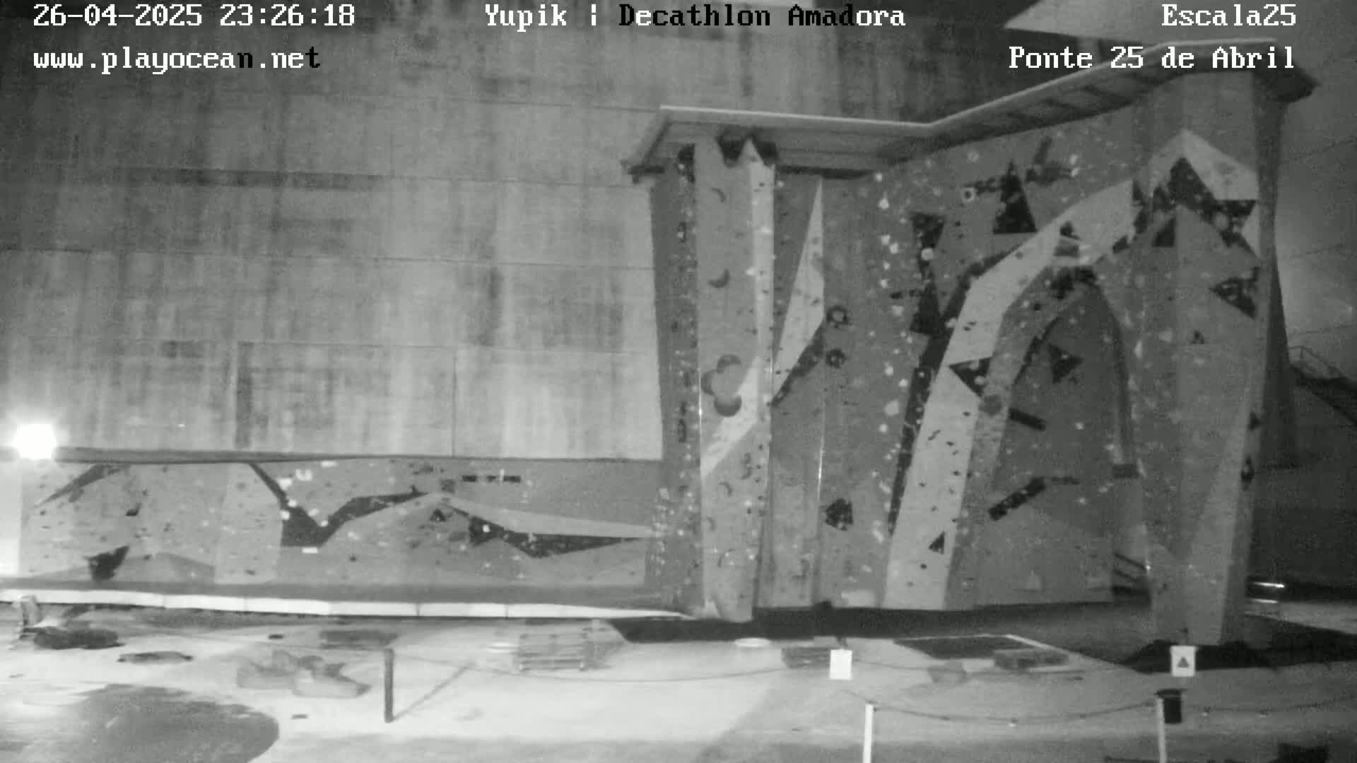 A black-and-white nighttime image shows an indoor climbing wall with various holds and textures.