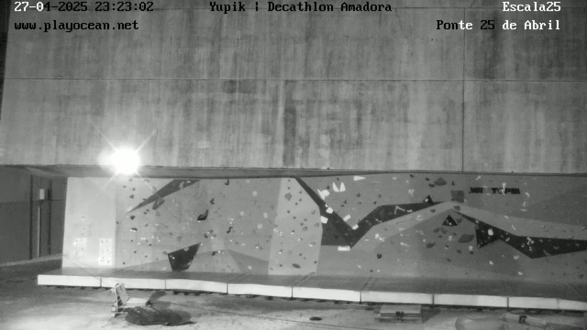 A nighttime, black and white image shows an outdoor climbing wall under a bright light.