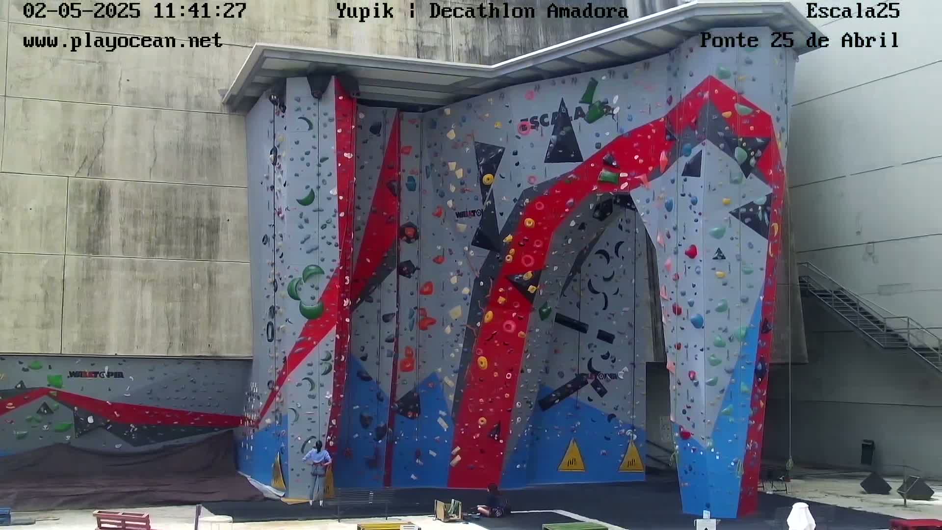 A large, colorful indoor climbing wall with several people near its base.