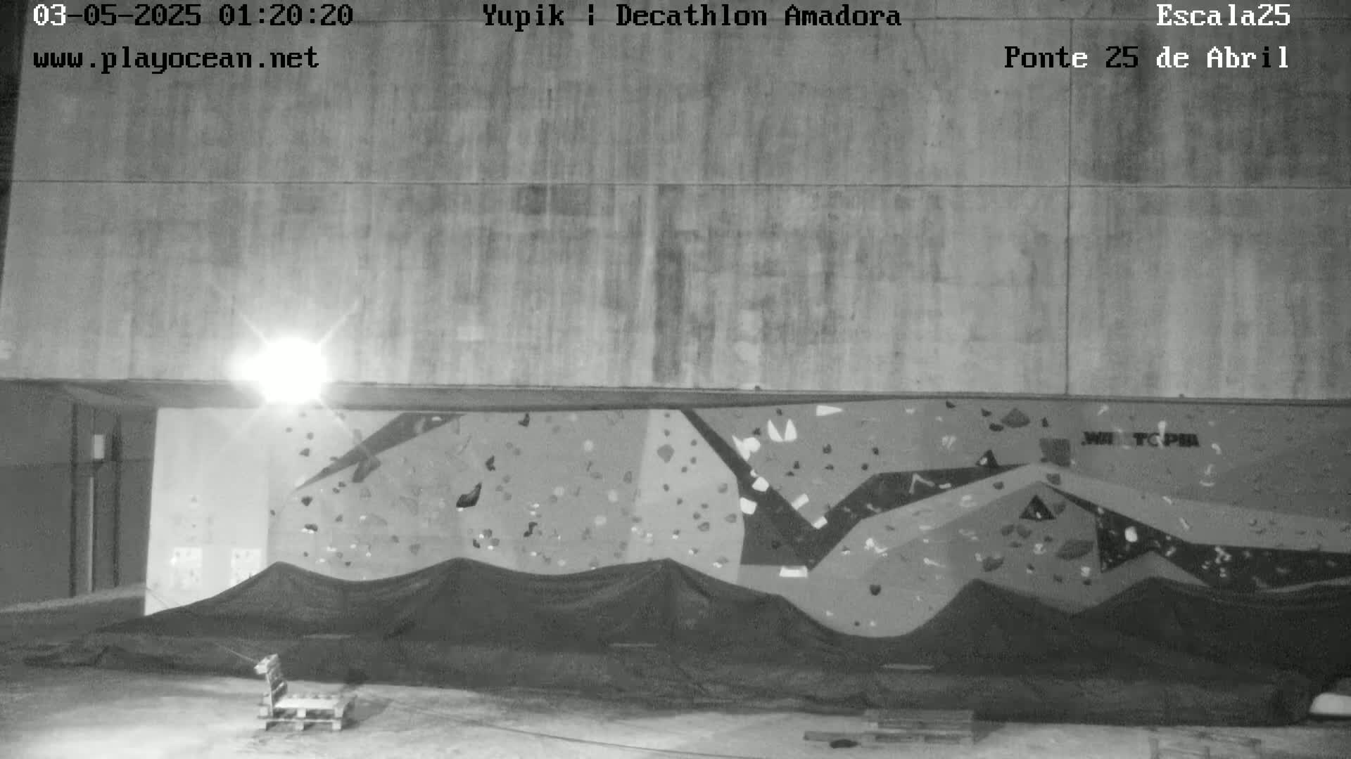 A black and white nighttime image shows an indoor climbing wall partially covered by a dark tarp.