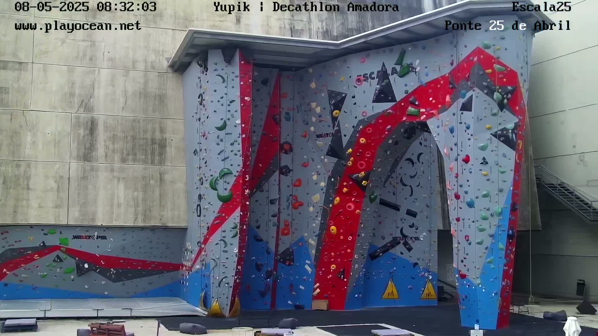 A large, colorful indoor climbing wall is situated outdoors on an overcast day.