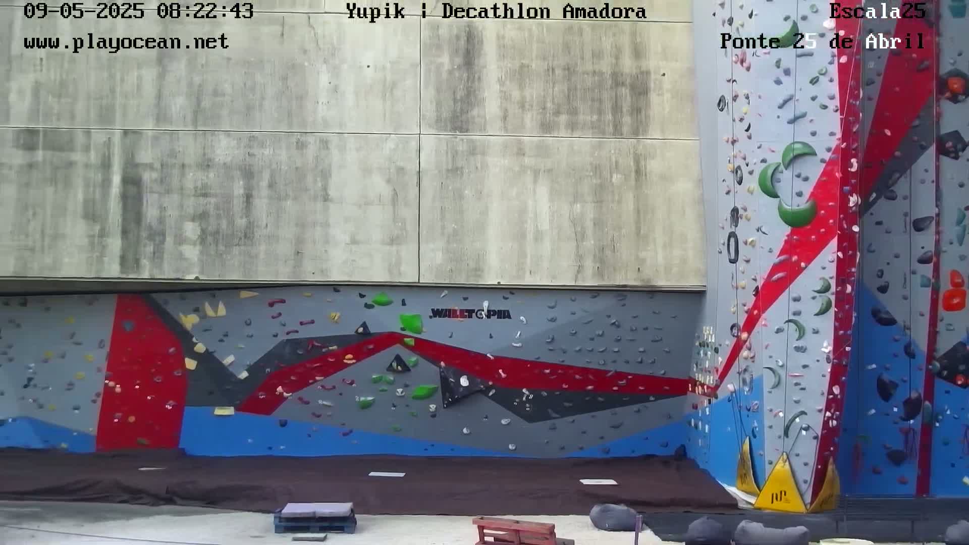 A large outdoor climbing wall with various colored holds is visible, under a cloudy sky.