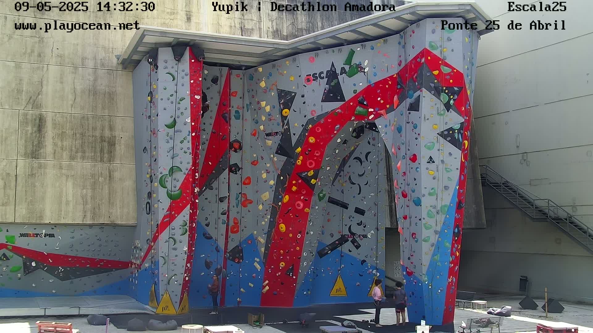 A large, colorful indoor climbing wall with several people standing at its base.