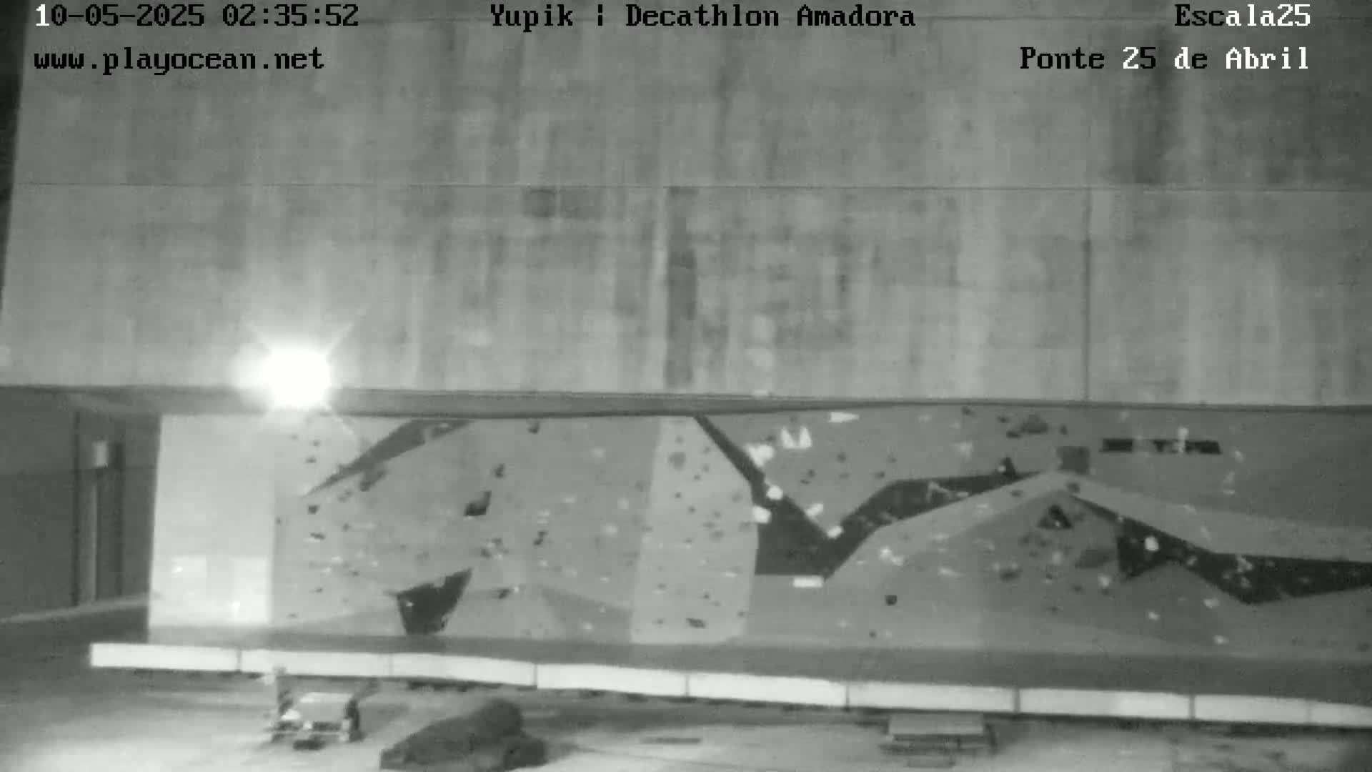 A grayscale nighttime image shows a large, indoor climbing wall under artificial light.