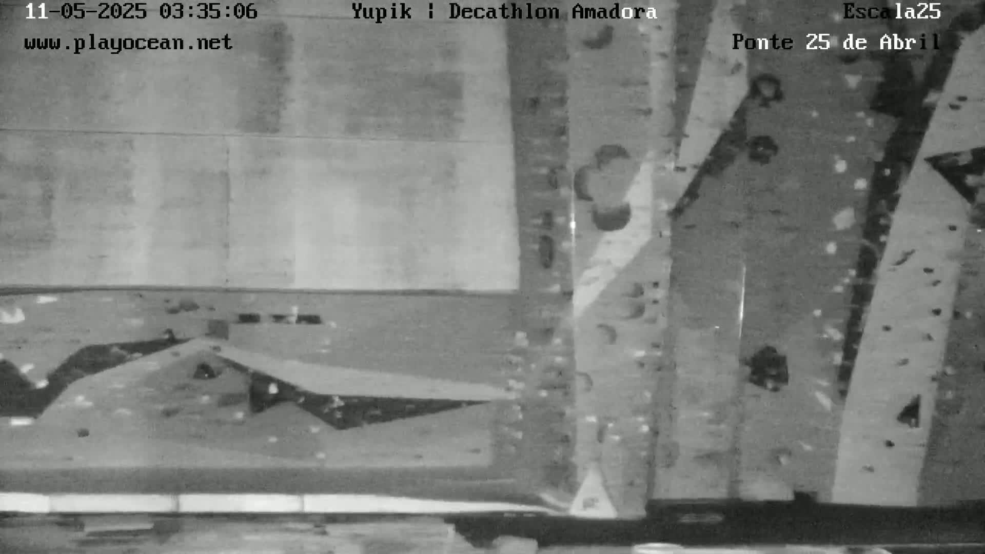 A grainy, black-and-white image shows an indoor climbing wall with various holds.
