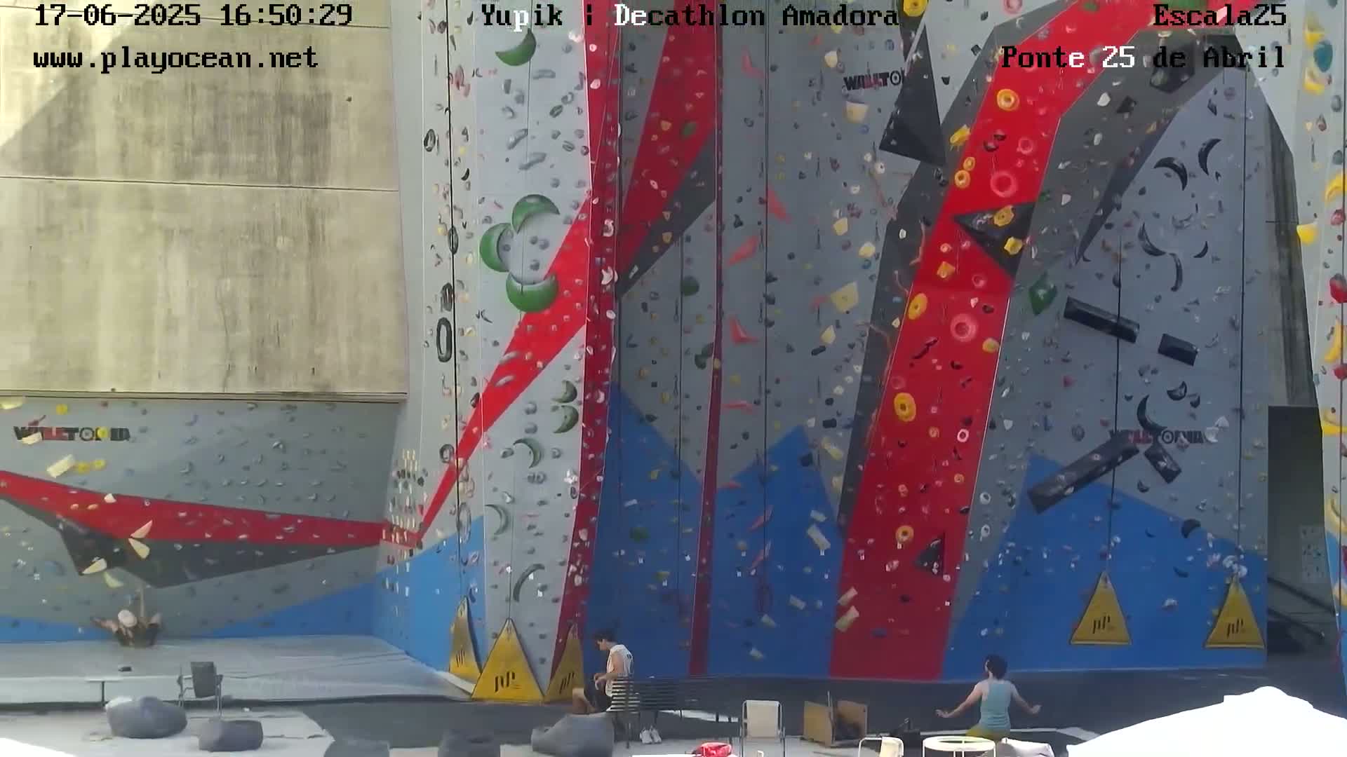 A large, colorful indoor climbing wall with several people near it on a sunny day.