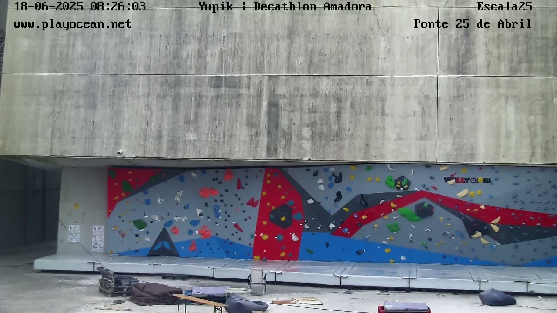 A large, colorful climbing wall is situated against a concrete building under an overcast sky.