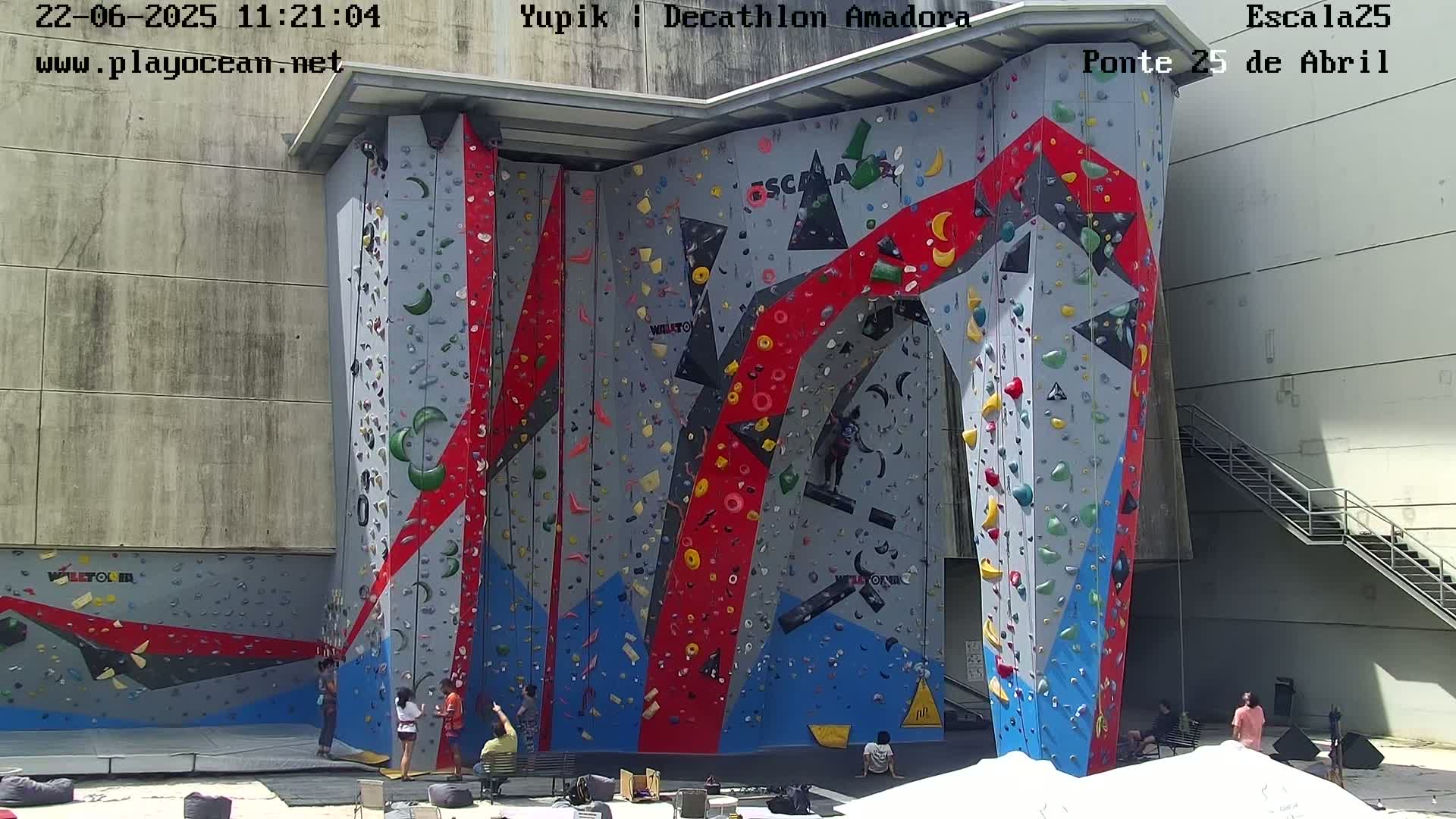 A large, colorful indoor climbing wall with several people climbing and watching.