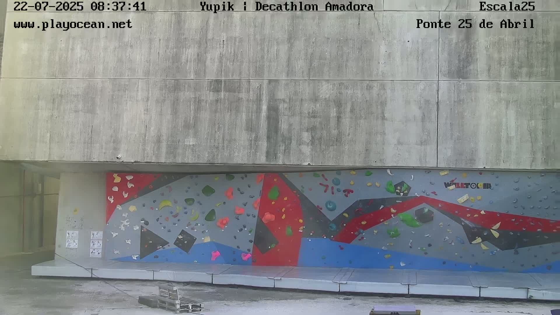 A colorful outdoor climbing wall is situated against a concrete building under overcast skies.