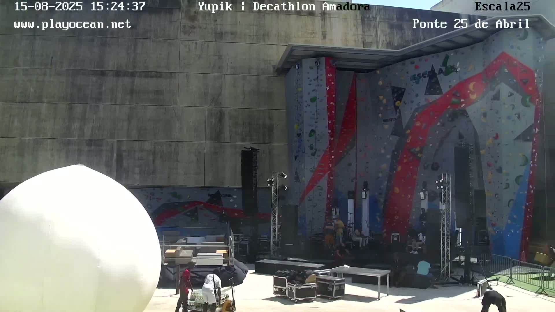 A large, brightly colored indoor climbing wall is shown at night, with a few people at its base.
