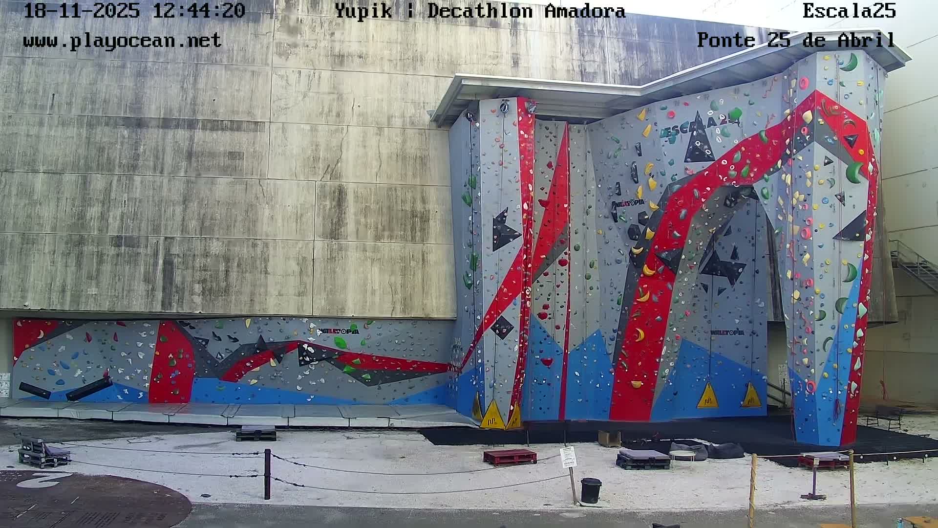 A large, brightly colored indoor climbing wall is shown at night, with a few people at its base.