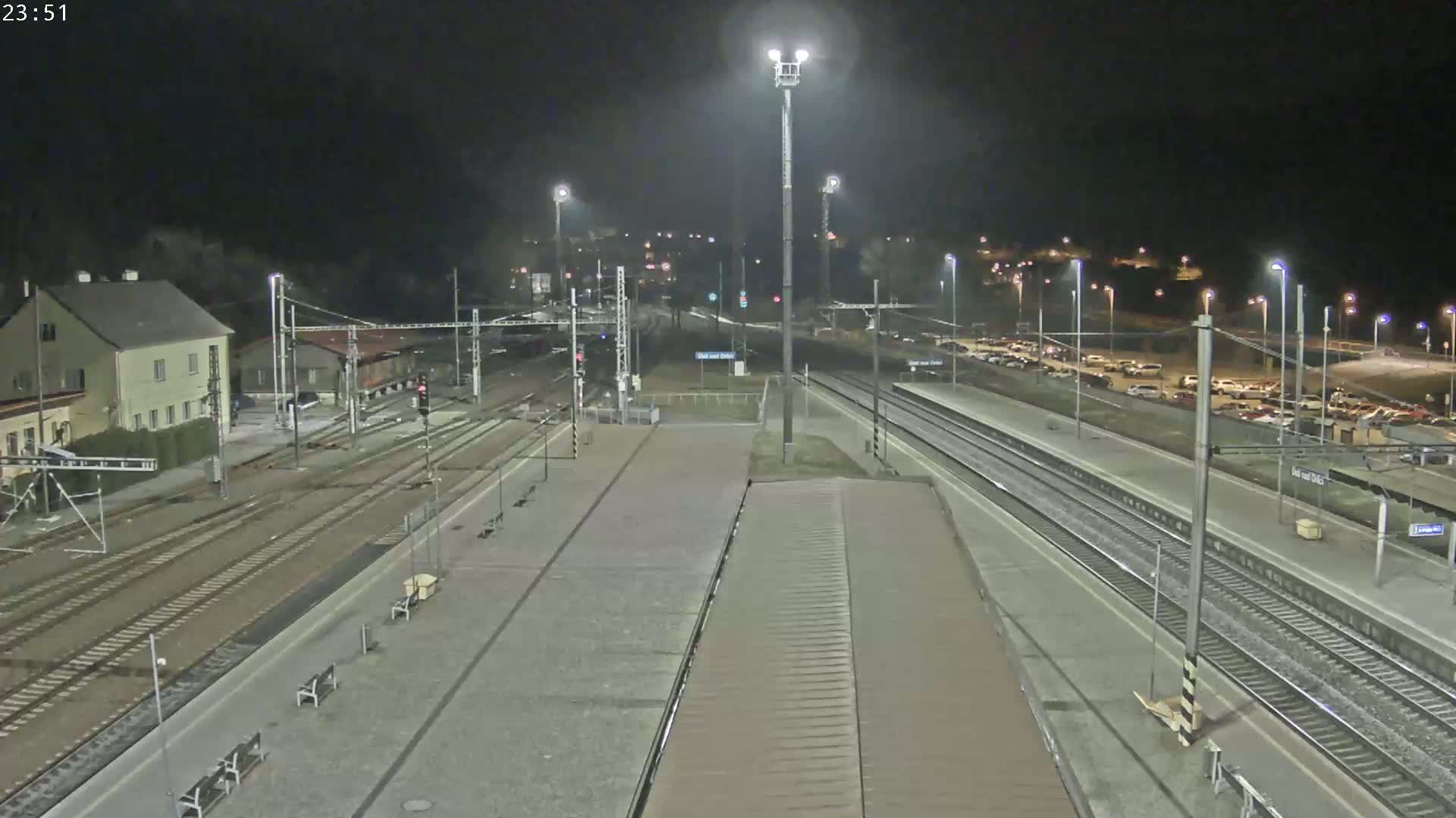 A nighttime view of a train station with multiple train tracks, a parking lot, and a building.