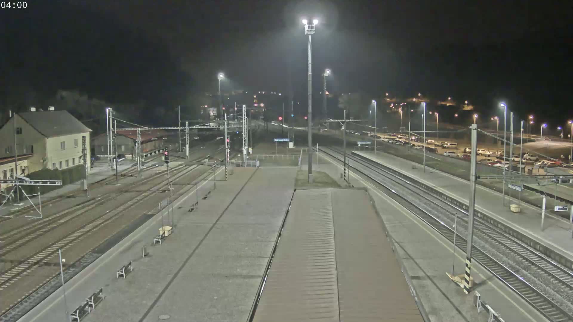 A nighttime view of a train station with multiple train tracks, a parking lot, and several buildings under a clear sky.