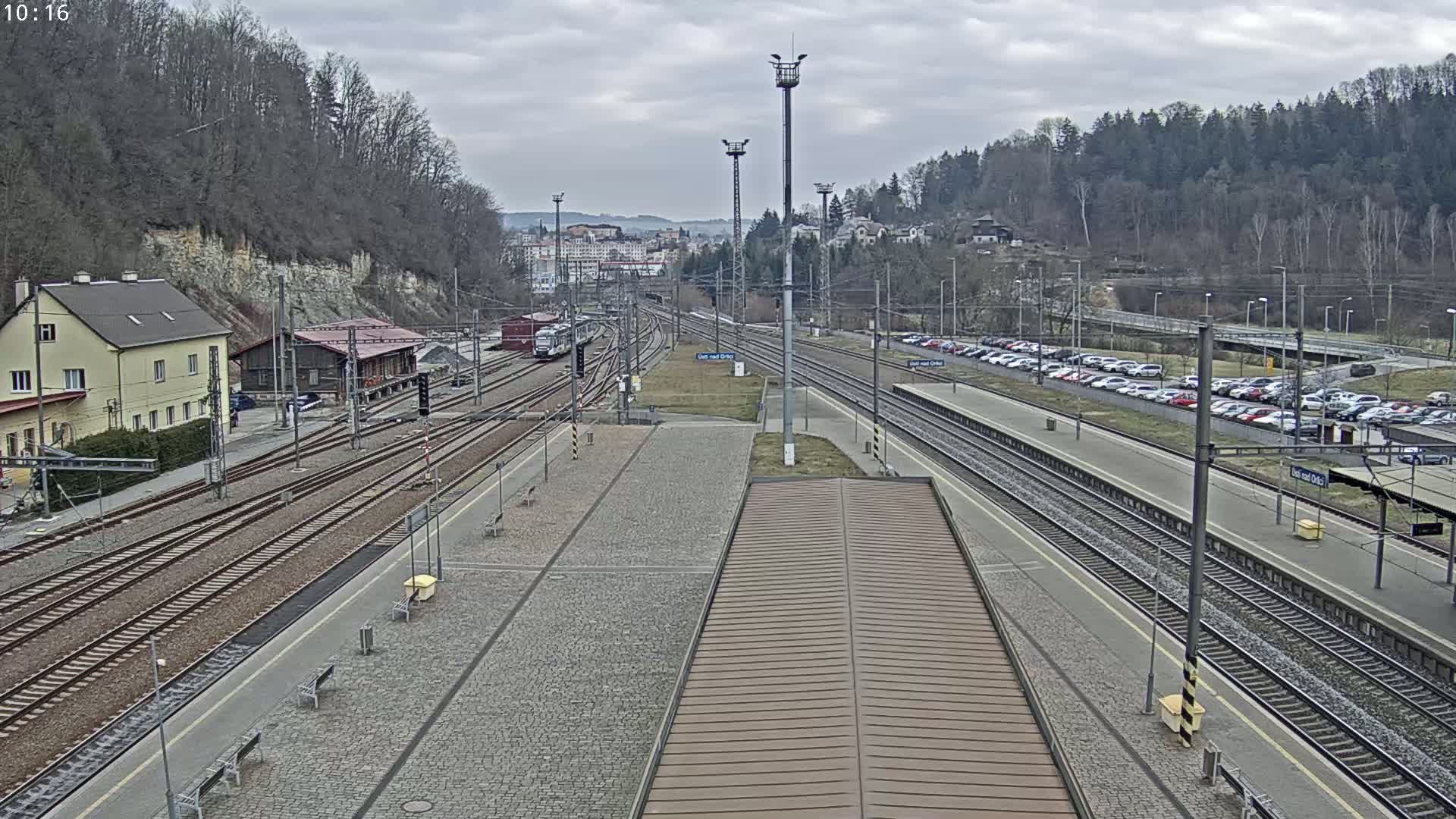 A train station with multiple train tracks, a large parking lot, and buildings under an overcast sky.