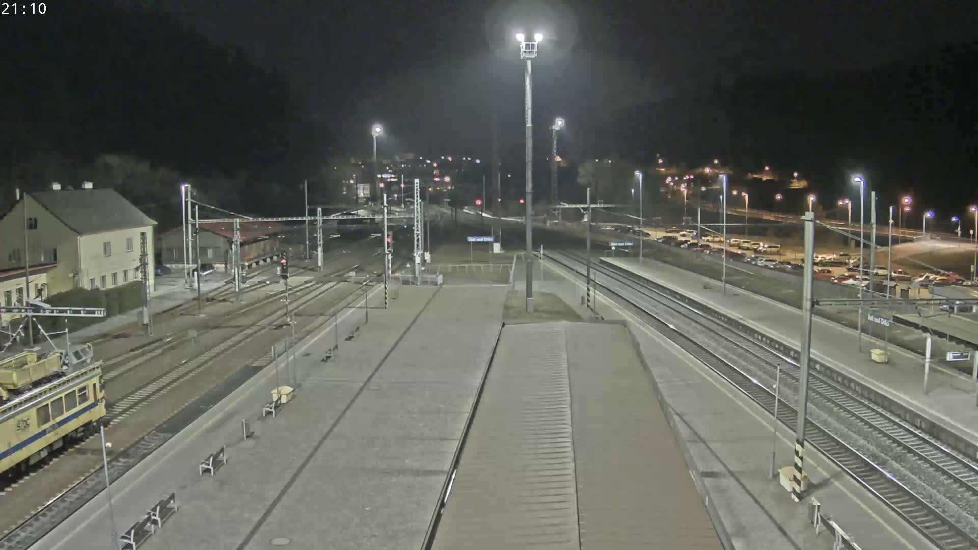 A nighttime view of a train station with multiple train tracks, a platform, and a train partially visible, under clear skies.