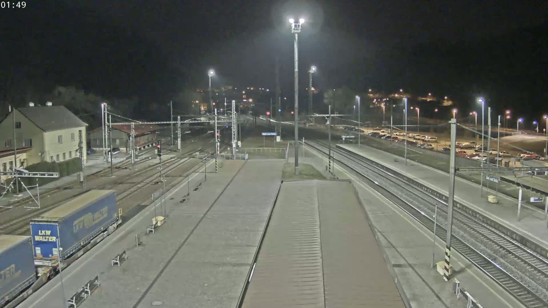 A nighttime view of a train station with multiple train tracks, a parking lot, and a building, under clear skies.