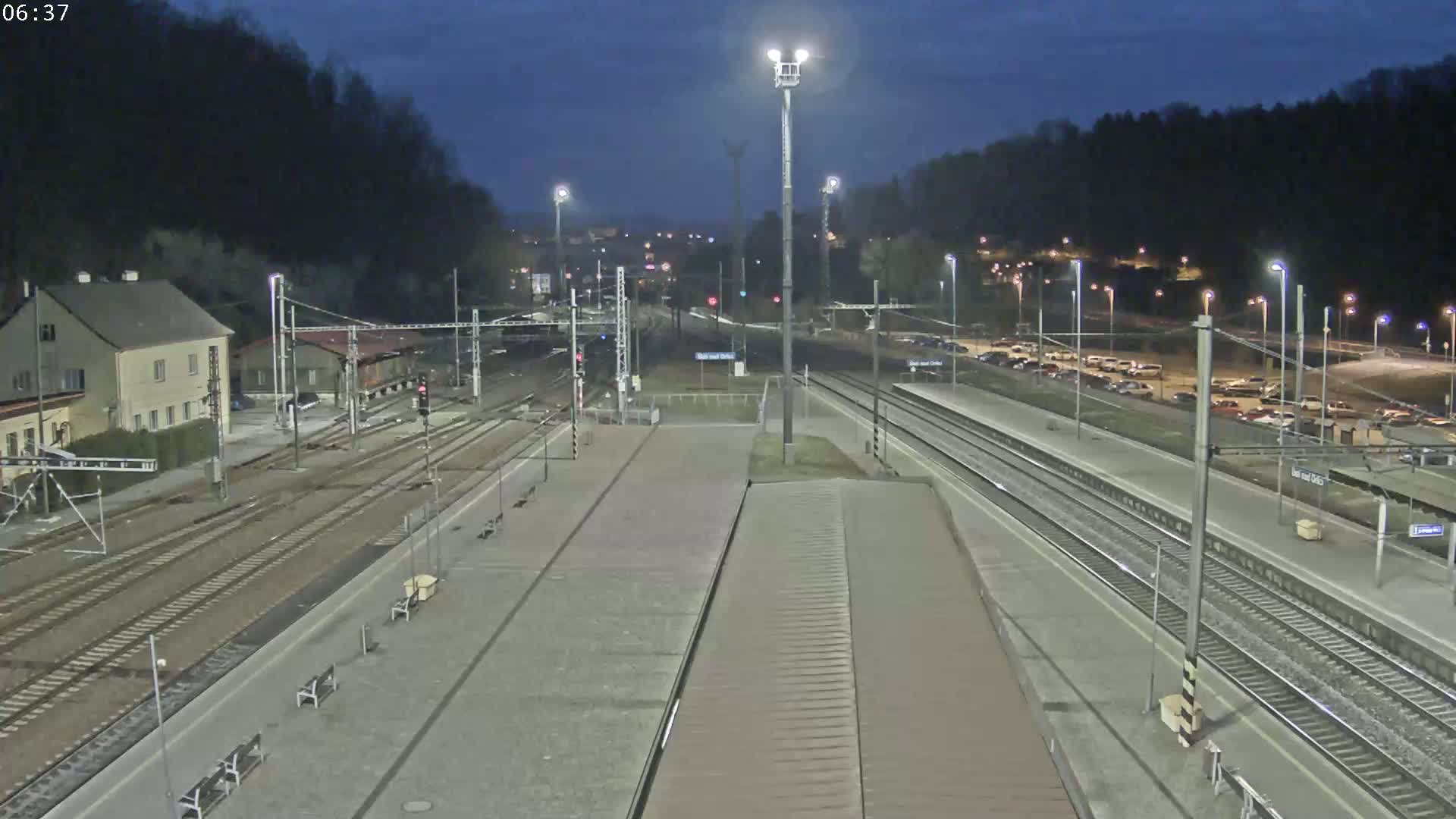 A nighttime view of a train station with multiple tracks, platforms, and a parking lot, under a dark, clear sky.