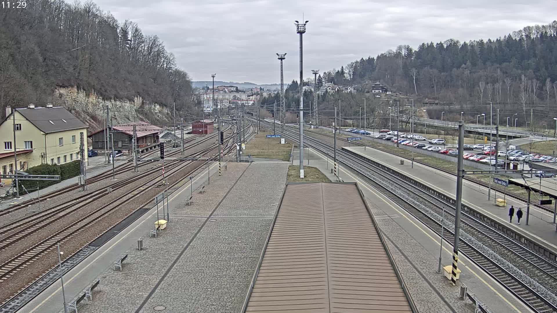 A train station with multiple tracks and a large parking lot is shown on an overcast day.