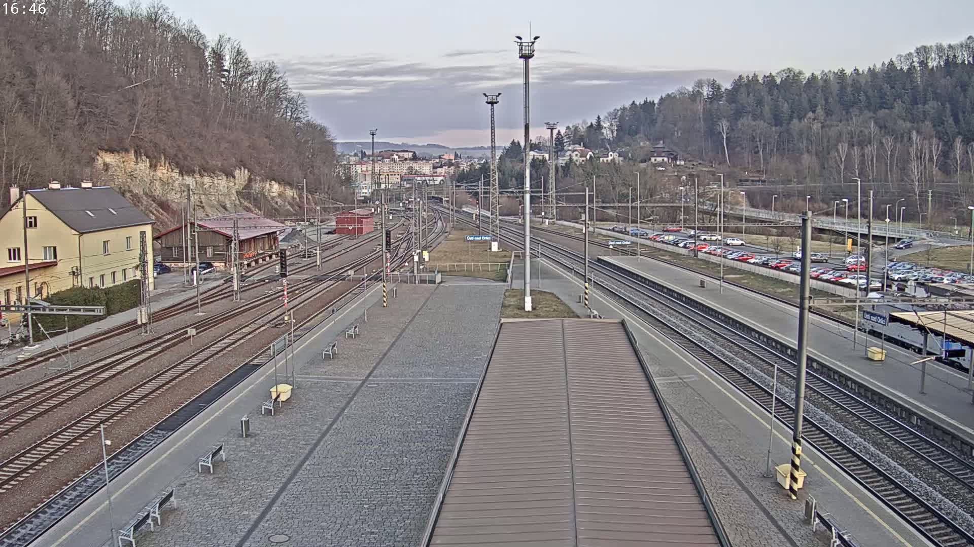 A train station with numerous tracks and parked cars is seen under an overcast sky.