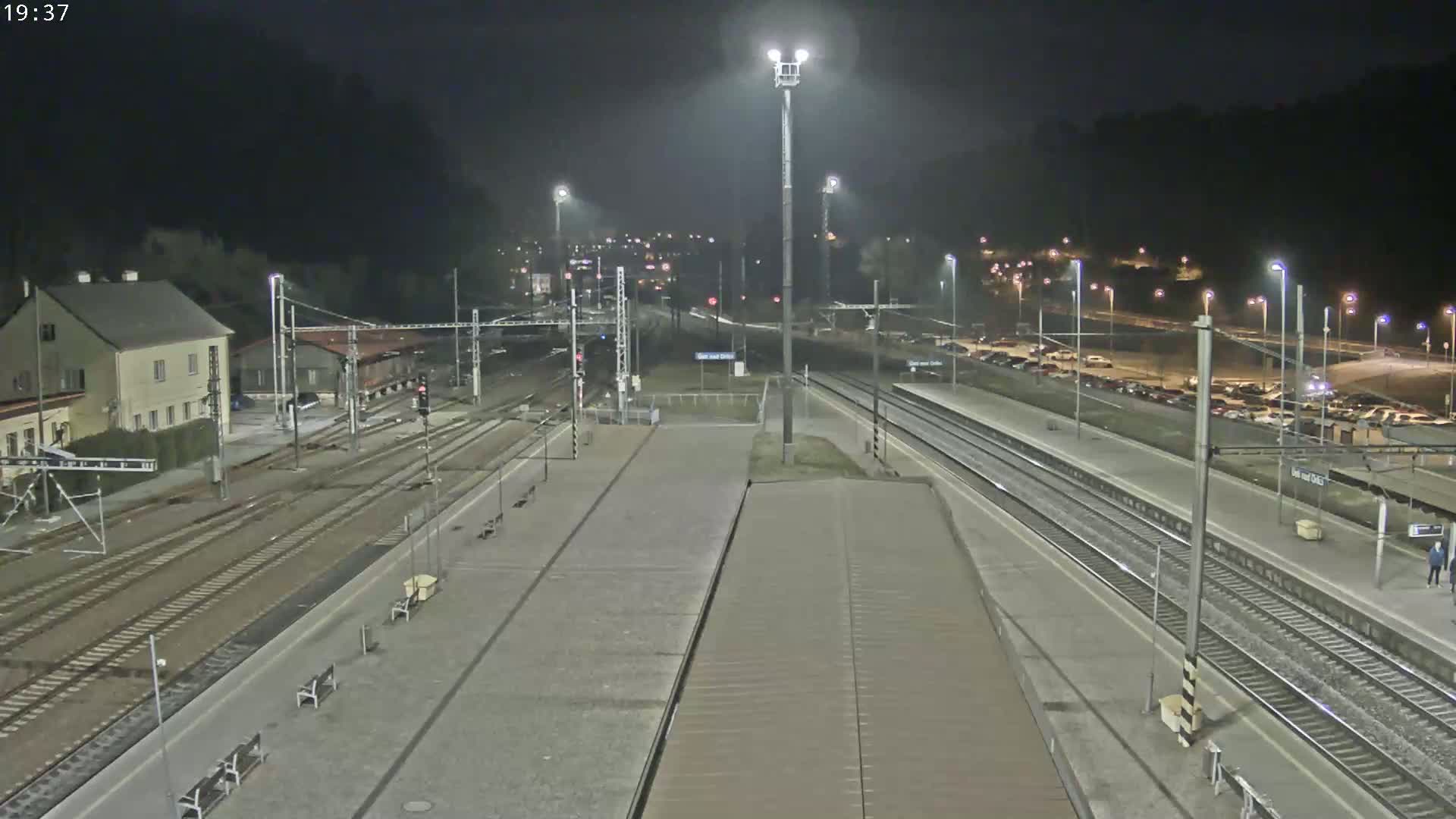 A nighttime view of a train station with multiple tracks, a parking lot, and a building, under dark, clear skies.