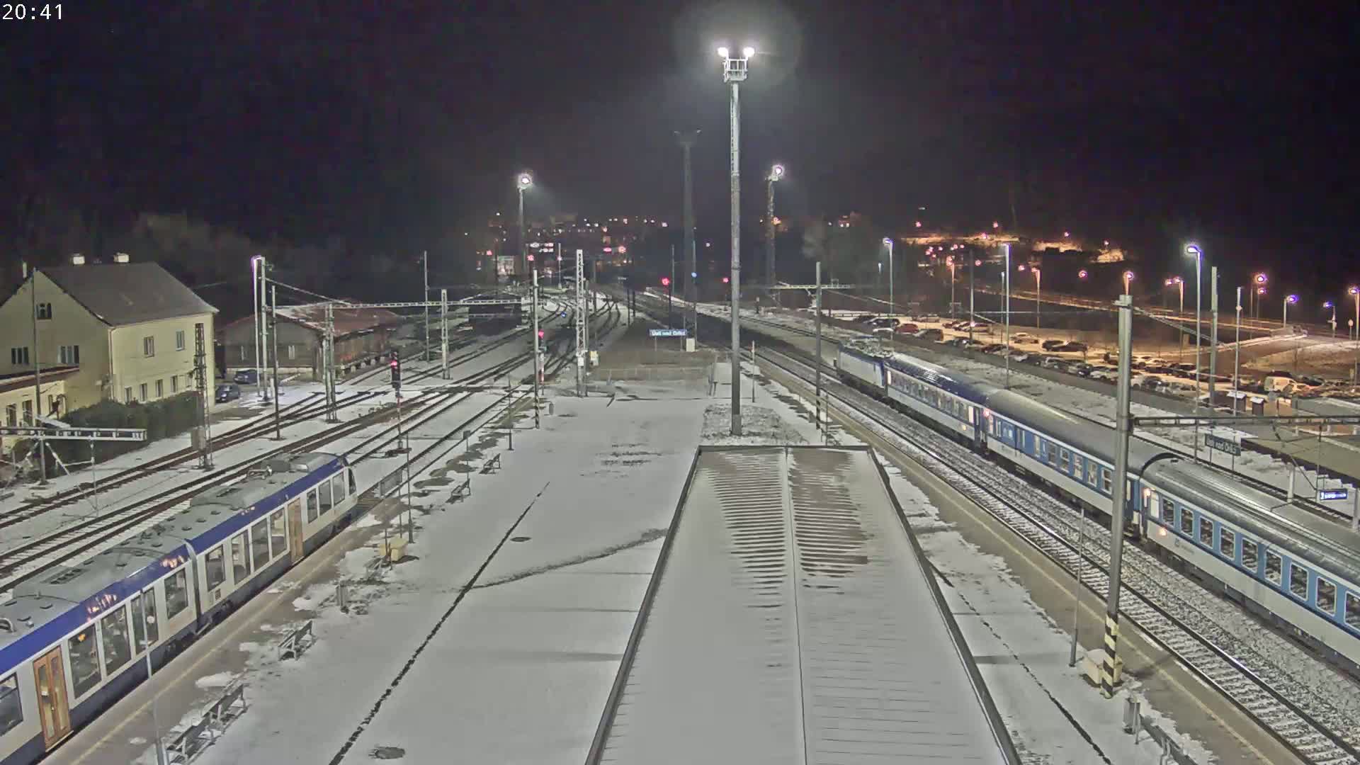 A snow-covered train station at night, with two trains visible on the tracks.