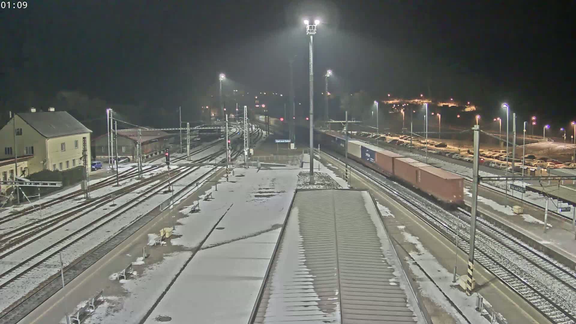 A freight train passes through a snow-covered train station at night.