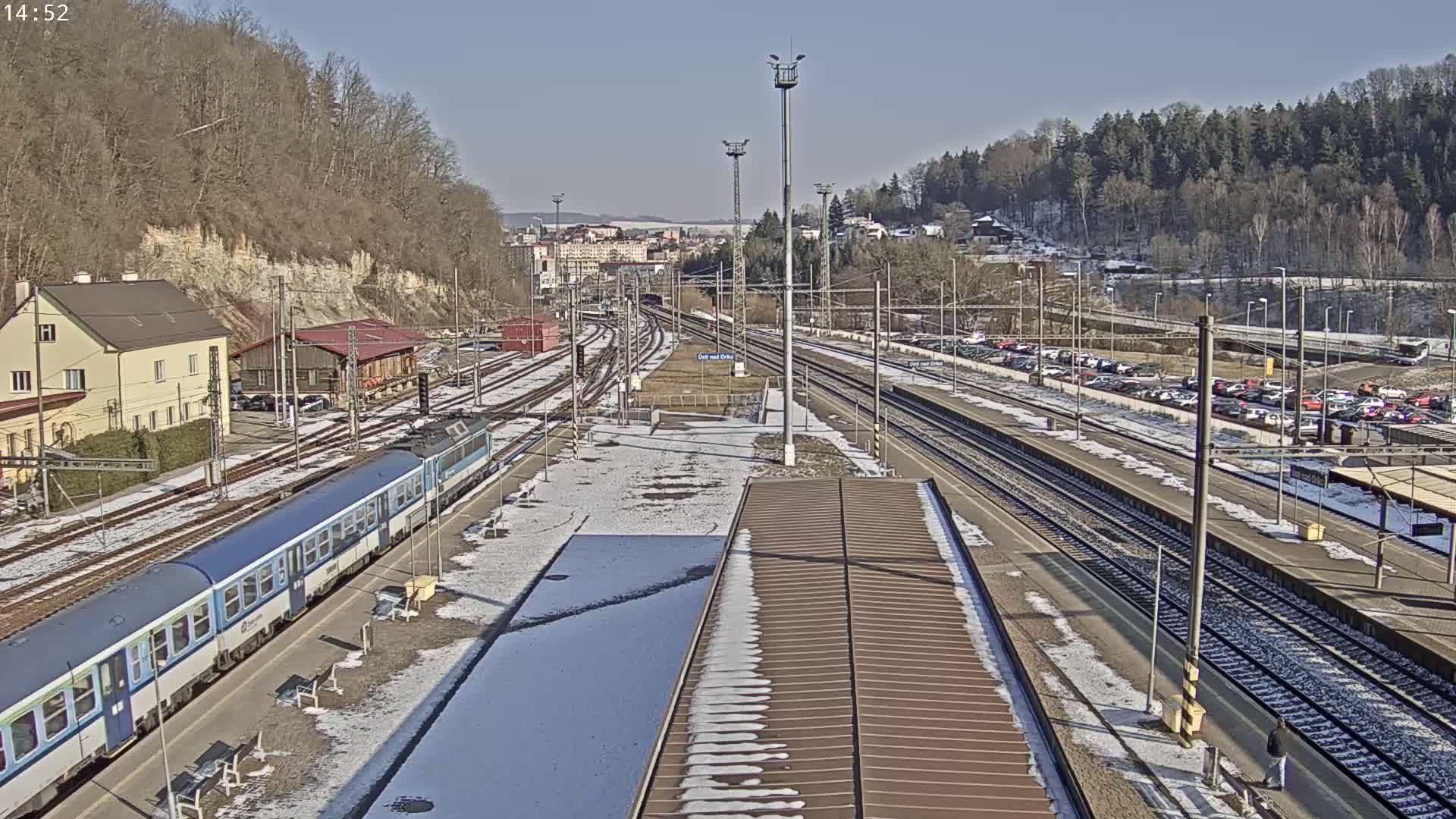 A train station on a sunny winter day with snow on the ground and a passenger train at the platform.