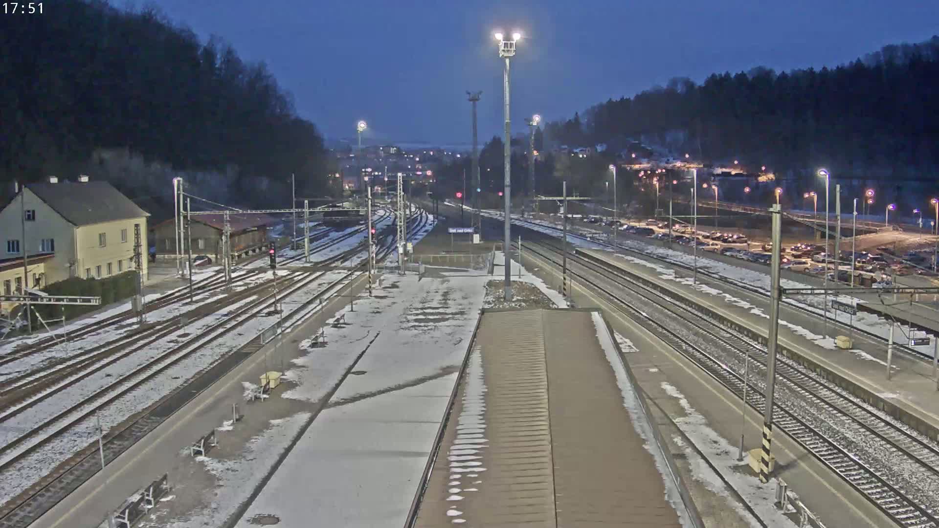 A snow-dusted train station at night, with multiple tracks and a parking lot visible.