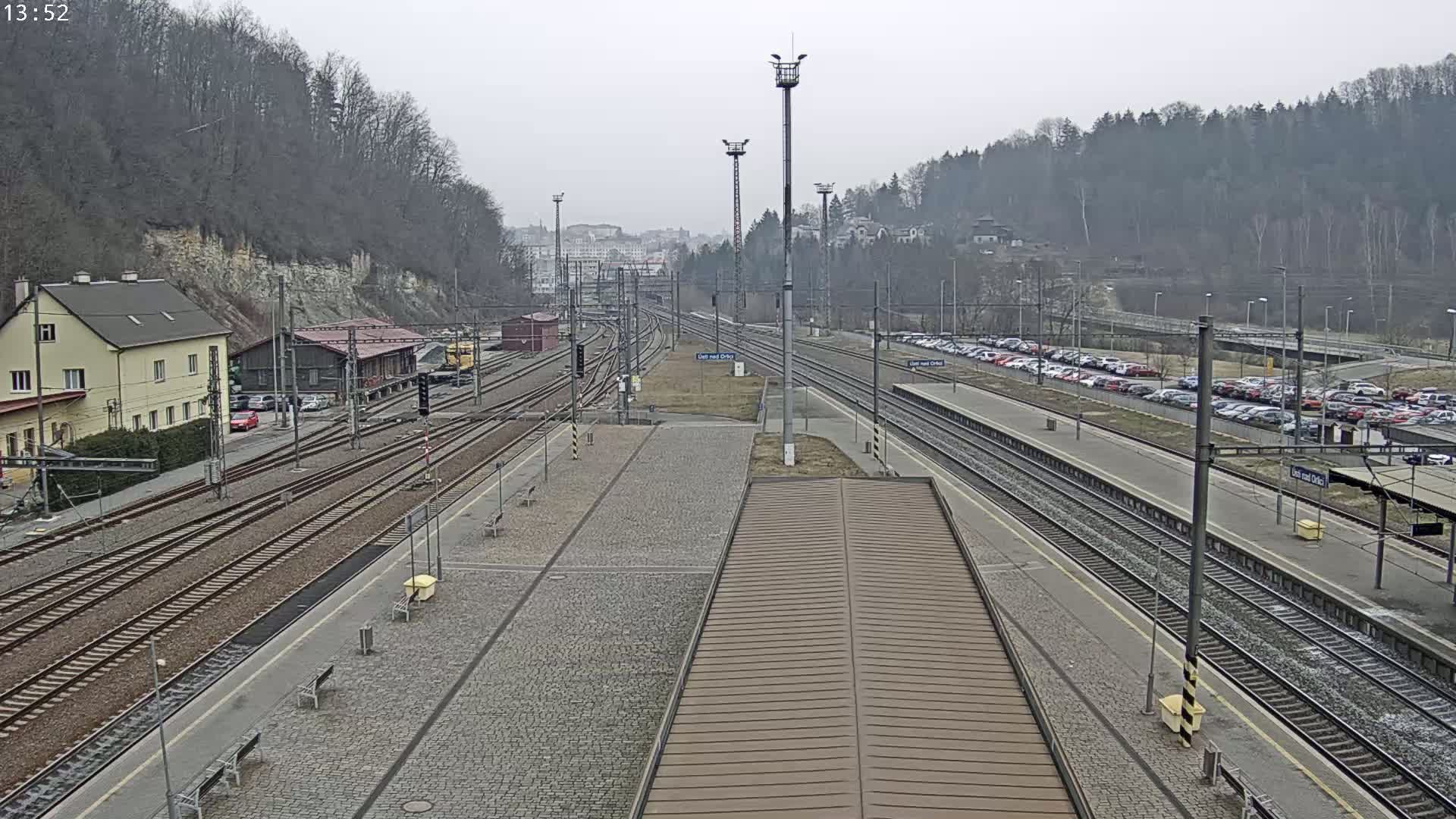 A train station with multiple train tracks and parked cars, under an overcast sky.